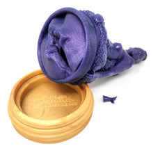 Load image into Gallery viewer, A silicone penetratable sculpture of Jet Setting Jasmine in dark, shimmery purple resting with her vulva side up on her gold stand silicone base, on a white background. The removable suction and cleaning plug is removed from the sculpture and next to the base.
