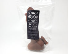 Load image into Gallery viewer, Realistic airbrushed dildo of King Noire&#39;s likeness with a charm version in a clear plastic bag, on a white background
