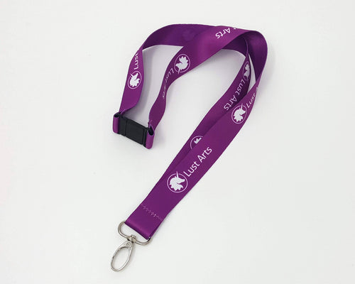 Photo of a medium-dark purple lanyard with the Lust Arts logo in white with a silver hook on an off-white background